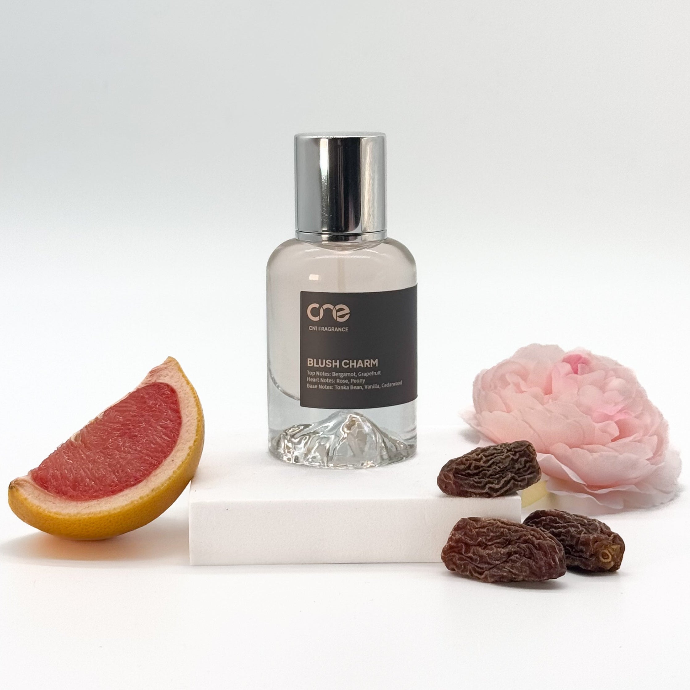 A bottle of Blush Charm by CN1 Fragrance, featuring a sleek, elegant design with a blush pink hue and a delicate floral pattern on the label.