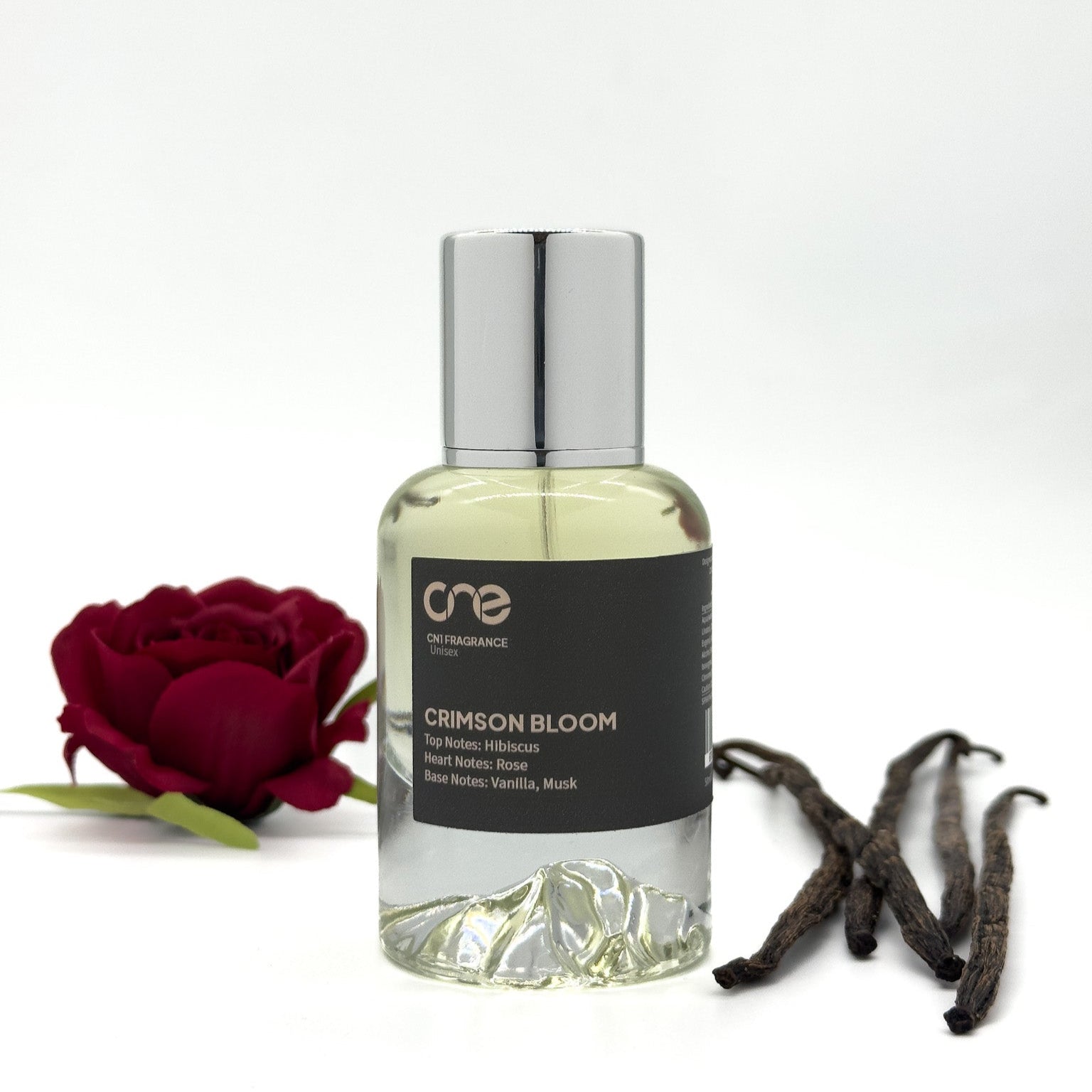 Crimson Bloom by CN1 Fragrance 50 ml clear bottle with deep red liquid and silver cap, surrounded by hibiscus and rose petals on white marble
